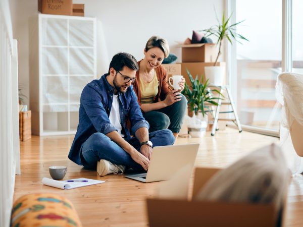 Happy couple relocating into a new home and using laptop while relaxing on the floor.
